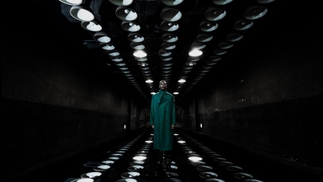 Photo of Jeff Mills wearing a long green coat and standing in a dark tunnel with lights