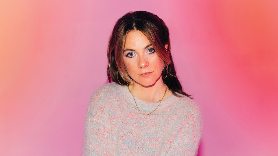 Photo of Bad Snacks wearing a pink and blue jumper against a pink background